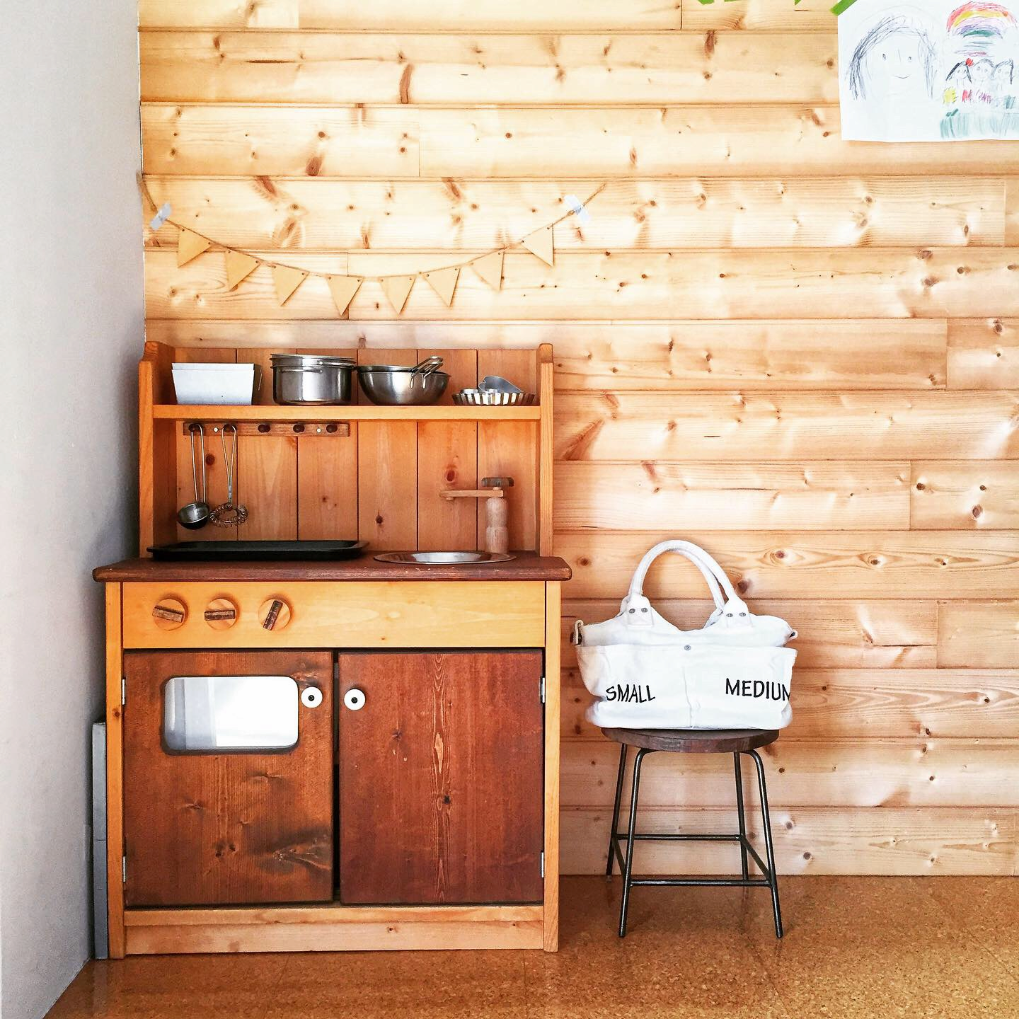 木製のおままごとキッチンと白いバッグがおいてある、木製の壁のスペース
