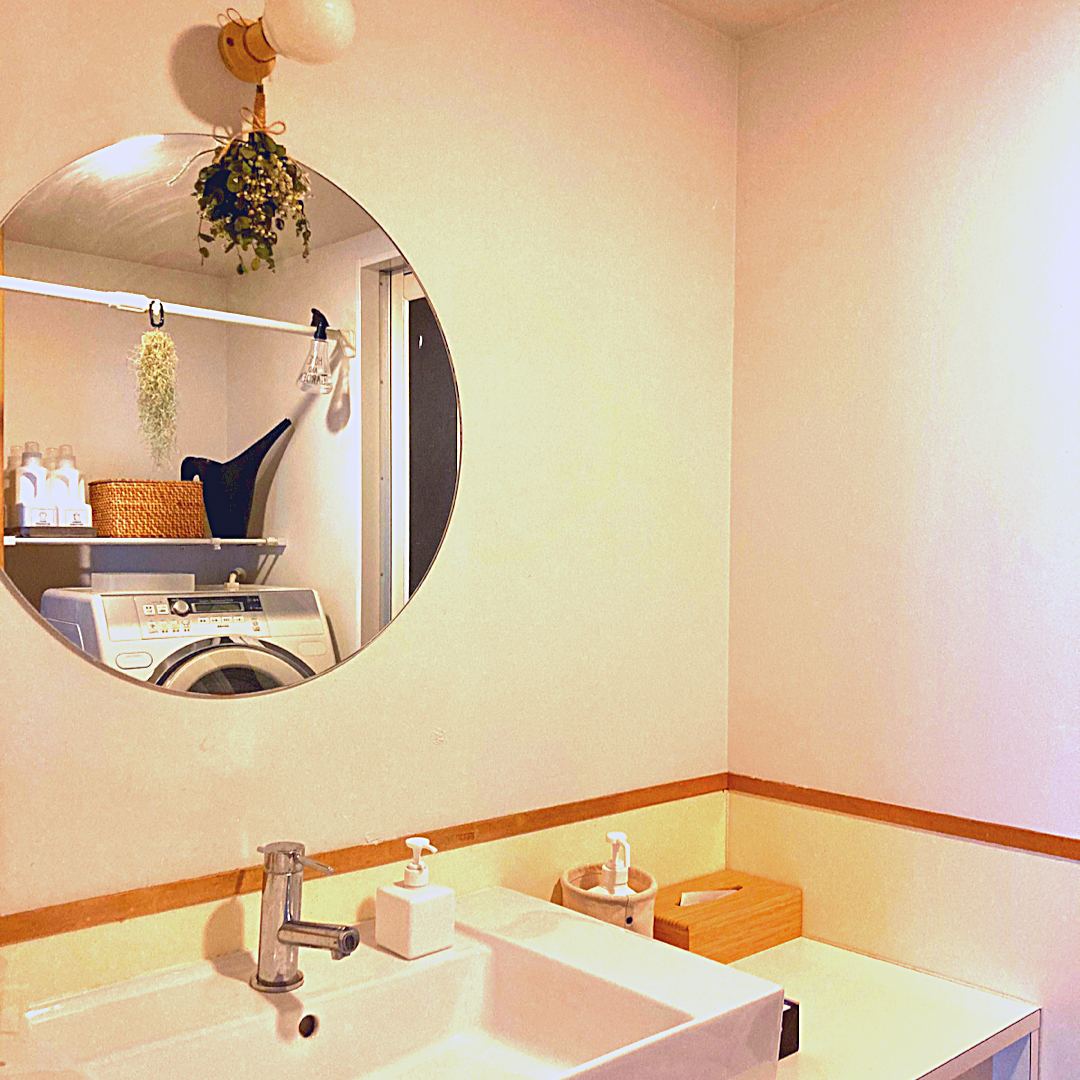 洗面台に設置されている丸い鏡。洗濯機とその上の棚が映っている