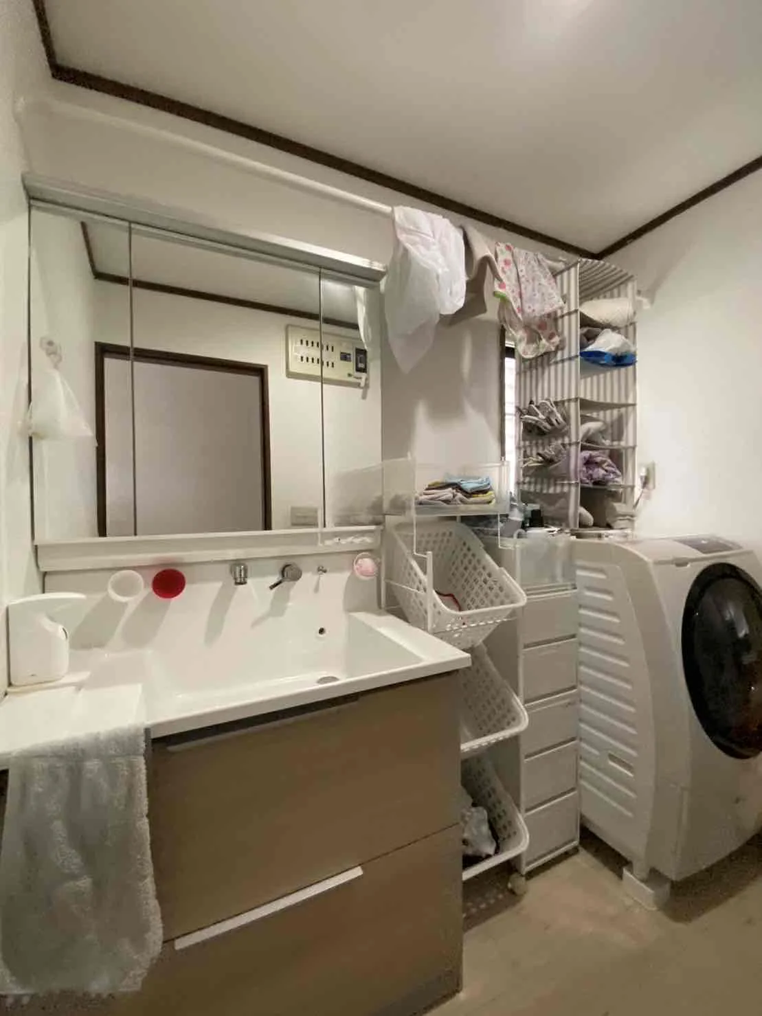 リフォーム前の洗面台。奥には洗濯用の棚とドラム式洗濯機が置かれている。