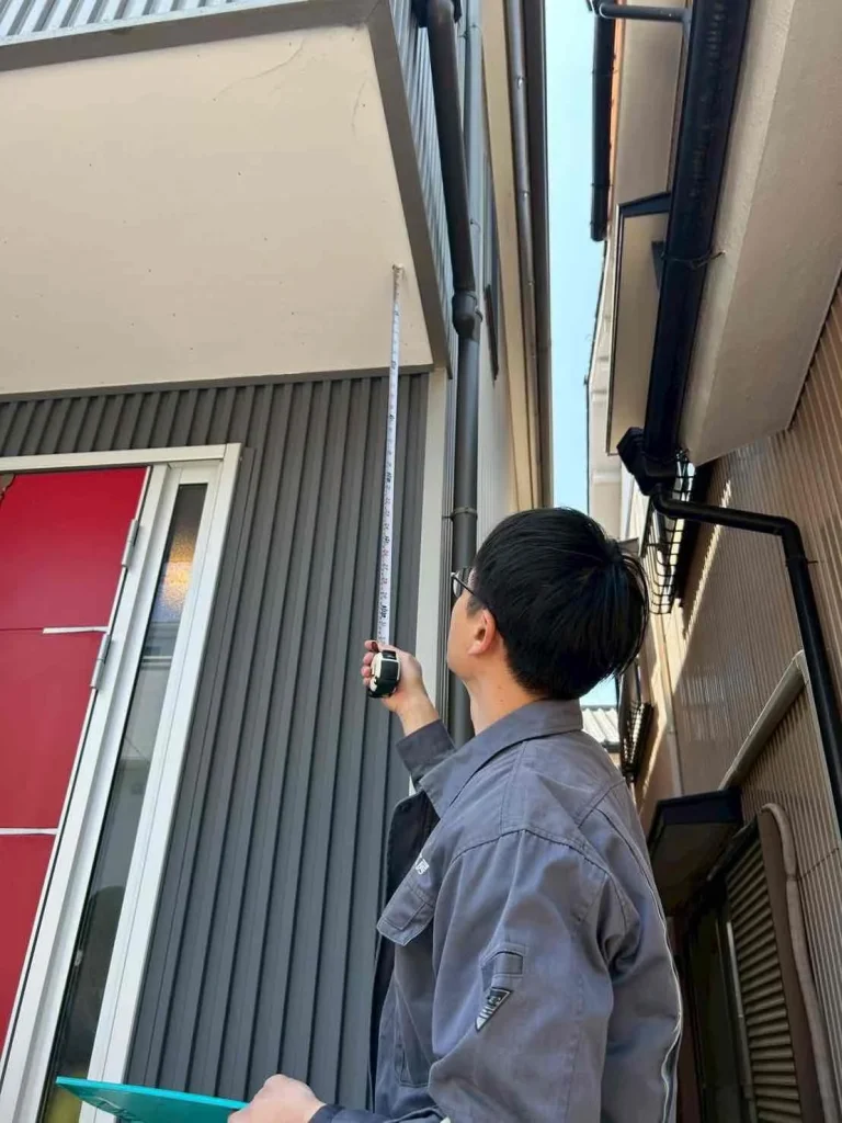 ベランダの下側をメジャーを持って点検する男性