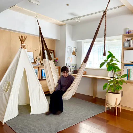 テントや観葉植物があるリビングでハンモックに座る笑顔の女性